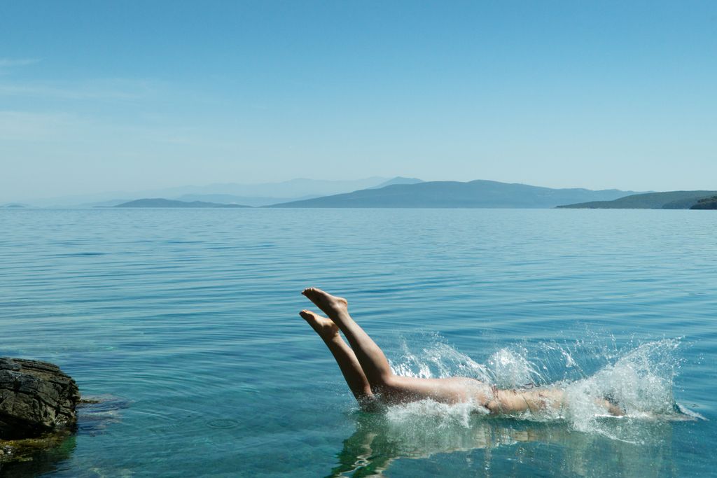 A person diving into a serene ocean, creating a splash under the clear blue sky.