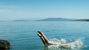 A person diving into a serene ocean, creating a splash under the clear blue sky.