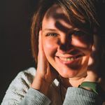 A woman smiling warmly with sunlight casting shadows across her face and hands.
