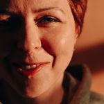 Close-up portrait of a smiling woman with red hair in warm light.